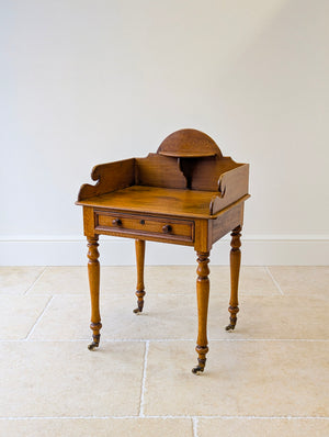 Antique Early Victorian country house oak side table with a scrolled gallery and raised shelf above a frieze drawer on turned legs with brass castors.