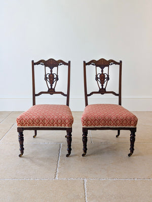 Antique Edwardian Sheraton Revival mahogany pair of salon chairs featuring anthemion marquetry, vase splats, red jacquard seats, and turned legs on brass castors.
