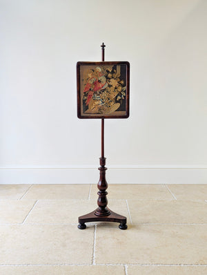 Antique William IV rosewood pole screen featuring a cushion-moulded frame enclosing a parrot needlepoint panel, set on a turned double-baluster stem and triform base.