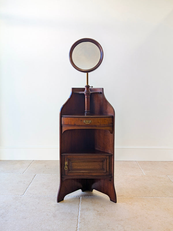 Antique Late Victorian mahogany corner shaving stand featuring a circular mirror on a brass stem, pivoting drawer, and cupboard, raised on splayed bracket feet.