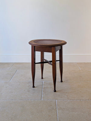Antique Edwardian Arts & Crafts oak occasional table with a circular oxblood panel top, square-tapered flared legs, swept X-stretcher, and turned ball feet.