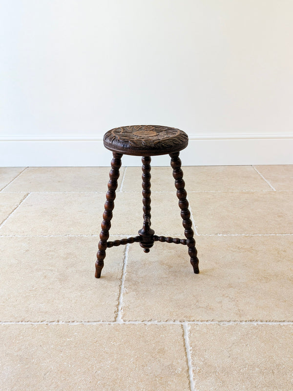 Antique late Victorian oak tripod stool featuring a carved sunflower top set over three splayed bobbin legs with a tripartite stretcher.