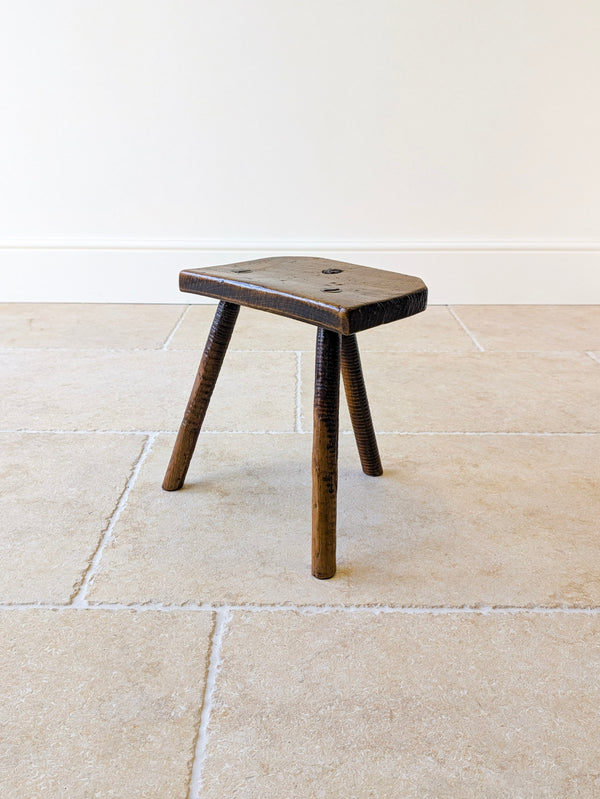 Antique Victorian elm and ash cutler's stool with a slab seat, canted corners, and wedged tenons, raised on three splayed ribbed legs.
