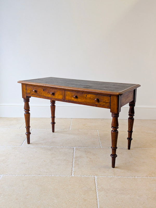 Antique Victorian mahogany writing table with a patinated black leathercloth inset writing surface over two drawers on ring-and-ball turned legs.