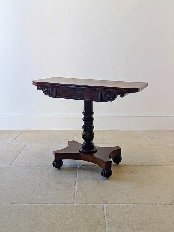 Antique William IV mahogany fold-over tea table featuring a boxwood-inlaid top, acanthus-carved pillar, and quadform platform base on gadrooned bun feet.