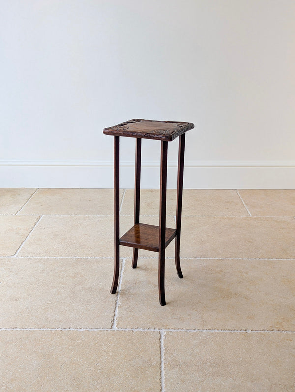 Antique Edwardian Arts and Crafts oak plant stand featuring a deeply carved square top, fixed undertier, and four slender square legs with splayed feet.