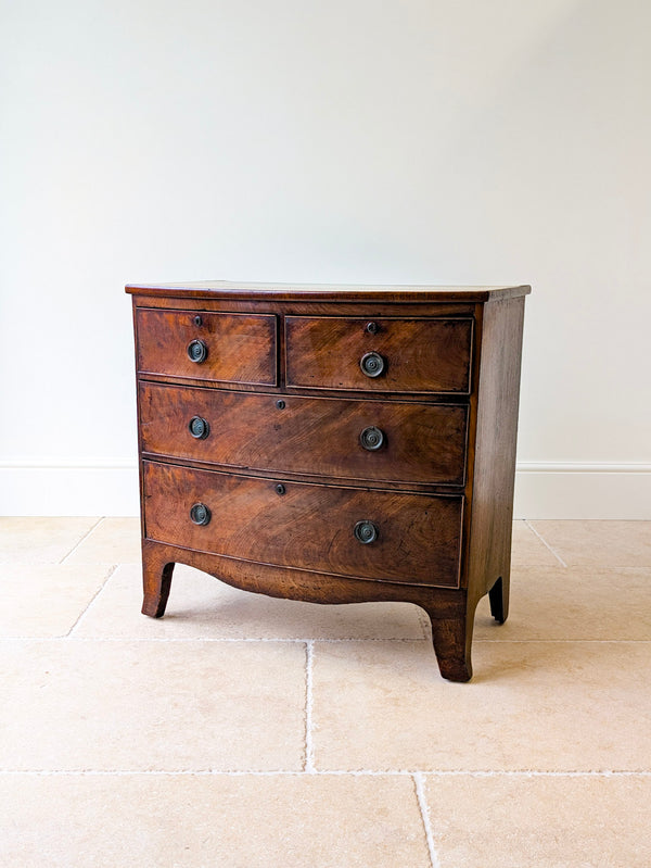 Antique George III flame mahogany bowfront chest of drawers with two short and two long graduated drawers, brass handles, and splayed bracket feet.