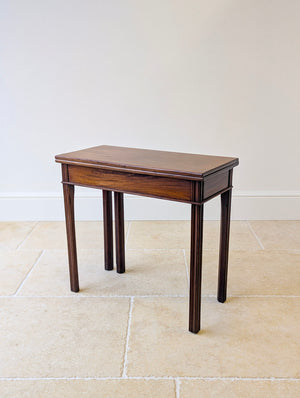 Antique George III mahogany fold-over tea table featuring a rectangular top with rounded edges and flame-veneered frieze, raised on vertically reeded square-tapered legs.