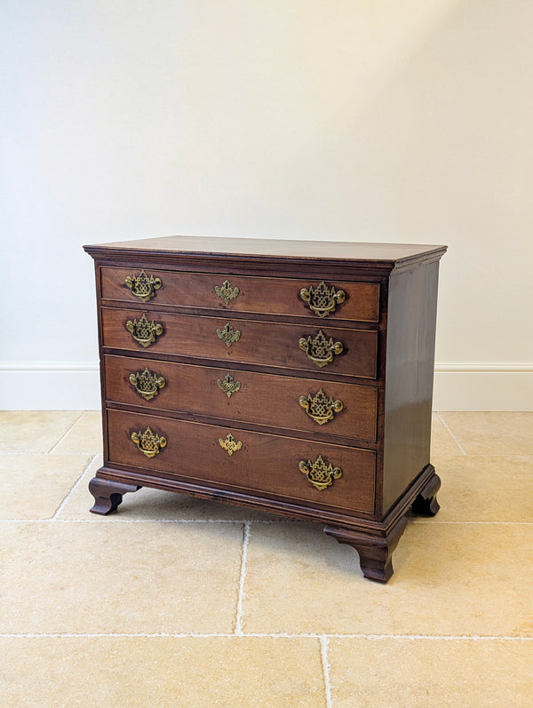 Antique George II mahogany chest of drawers with a single‑plank moulded top, four graduated cockbeaded drawers with pierced fret brass hardware, and ogee bracket feet.