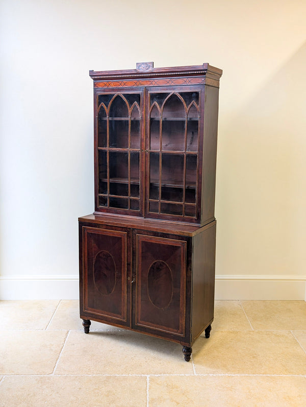 Antique George III mahogany cabinet bookcase with Gothic astragal glazed doors above a cupboard with flame mahogany oval reserves, raised on turned feet.