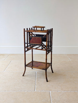 Antique Victorian bamboo canterbury magazine stand featuring hand-painted lacquer panels and a divided upper rack, raised on out-swept legs with brass foot caps.