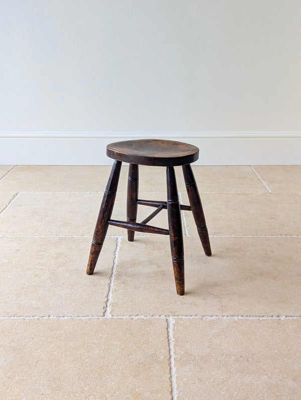 Antique Mid-Victorian solid English oak country low stool featuring a dished oval seat on raked tapered legs with incised ring collars and turned H-stretcher.
