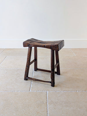 Antique Georgian vernacular oak low stool featuring a carved single-slab saddle seat over four splayed legs with staggered pegged stretchers.