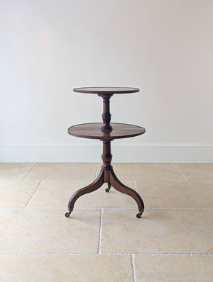 Antique Regency mahogany drop-leaf two-tier dumb waiter with twin graduated reeded platforms, turned central pillar, and reeded tripod legs on brass castors.