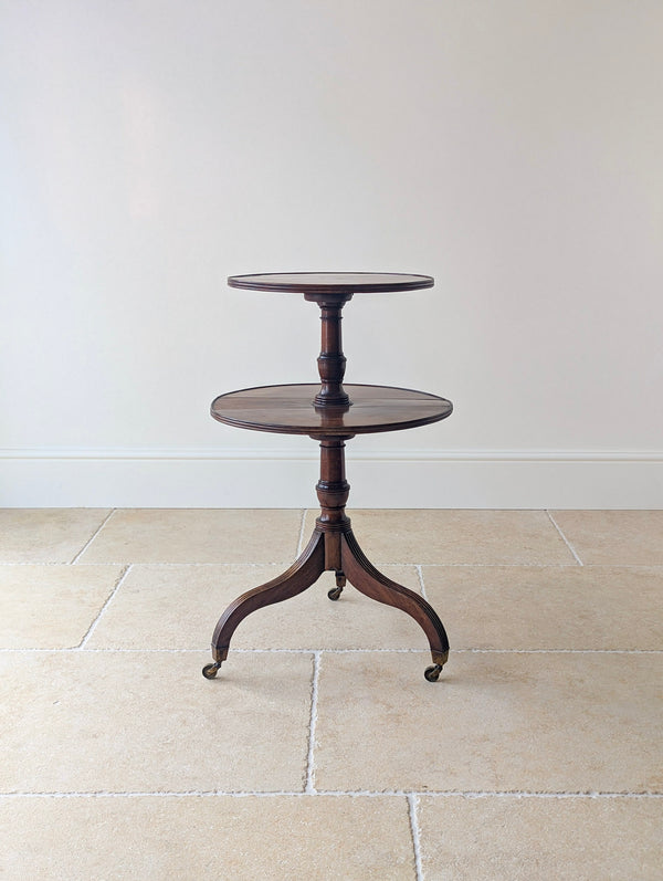 Antique Regency mahogany drop-leaf two-tier dumb waiter with twin graduated reeded platforms, turned central pillar, and reeded tripod legs on brass castors.