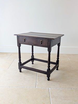 Antique William and Mary oak single-drawer side table with a two-plank top, brass teardrop handles, turned baluster legs, box stretcher, and ball feet.