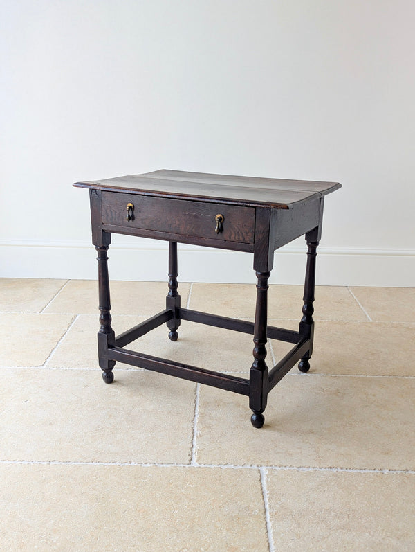 Antique William and Mary oak single-drawer side table with a two-plank top, brass teardrop handles, turned baluster legs, box stretcher, and ball feet.