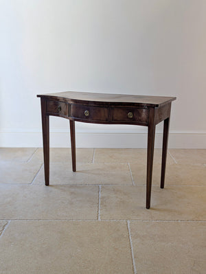 Antique George III mahogany serpentine side table with three conforming frieze drawers and brass patera ring handles, raised on four square tapered legs.