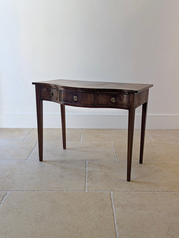 Antique George III mahogany serpentine side table with three conforming frieze drawers and brass patera ring handles, raised on four square tapered legs.