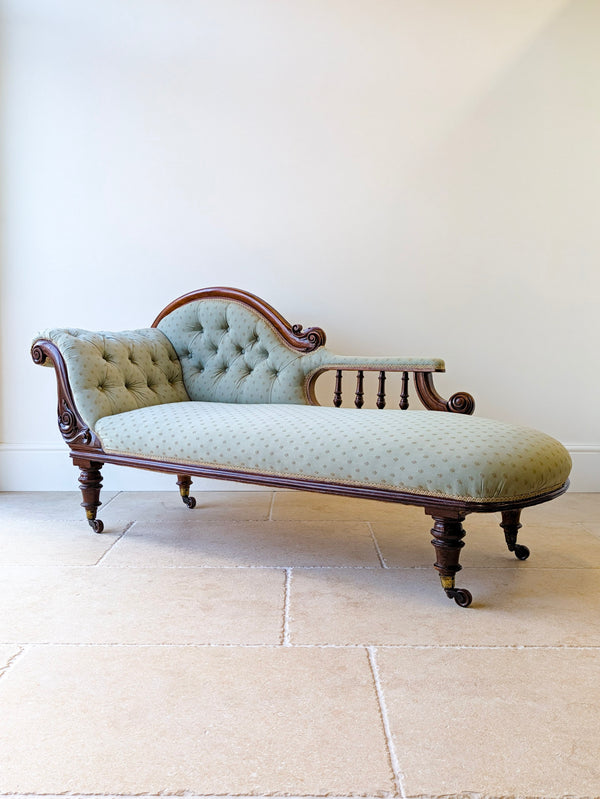 Antique Victorian mahogany chaise longue with buttoned sage upholstery, open spindle gallery arm, and turned legs on brass and ceramic castors.
