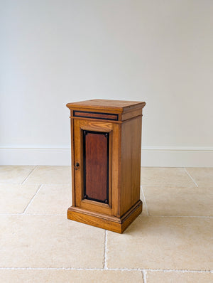 Antique Victorian oak bedside cabinet with ebonised and gilt‑detailed single door enclosing a central mahogany panel on a moulded plinth base