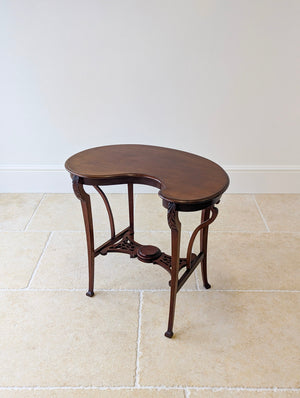 Antique Edwardian Art Nouveau mahogany side table featuring a shaped moulded top and pierced lower tier with curved decorative braces on slender carved legs.