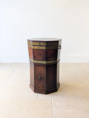 Antique George III mahogany octagonal cellaret featuring brass banding, inlaid crossbanded lid, side handles, lead-lined interior, and matching cupboard base on a stepped plinth.