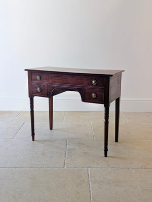 Antique Regency mahogany kneehole writing table with three cockbeaded drawers, central arched kneehole, turned front legs, and plain square tapered rear legs.