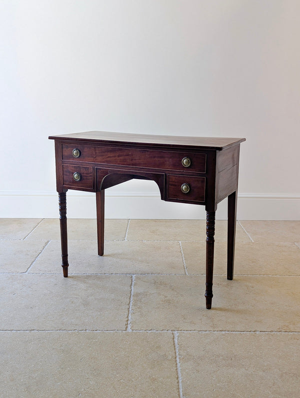 Antique Regency mahogany kneehole writing table with three cockbeaded drawers, central arched kneehole, turned front legs, and plain square tapered rear legs.