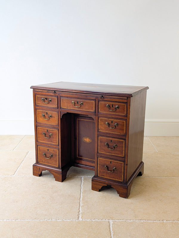 Warm mahogany kneehole desk featuring satinwood crossbanding, oval shell inlays and nine drawers with a recessed cupboard on bracket feet.
