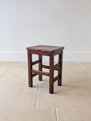 Antique Edwardian country pine stool with red paint finish, a hollowed rectangular top and square-section legs united by stretchers.