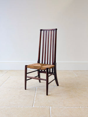 Antique Arts and Crafts stained beech high-back side chair featuring seven vertical slats, a natural rush seat, turned front posts, and splayed rear legs.

