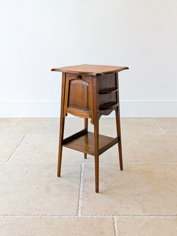 Antique Arts & Crafts oak occasional table with a flared pagoda top, drop-front cabinet, integrated pipe rack, and lower tier on square-tapered splayed legs.